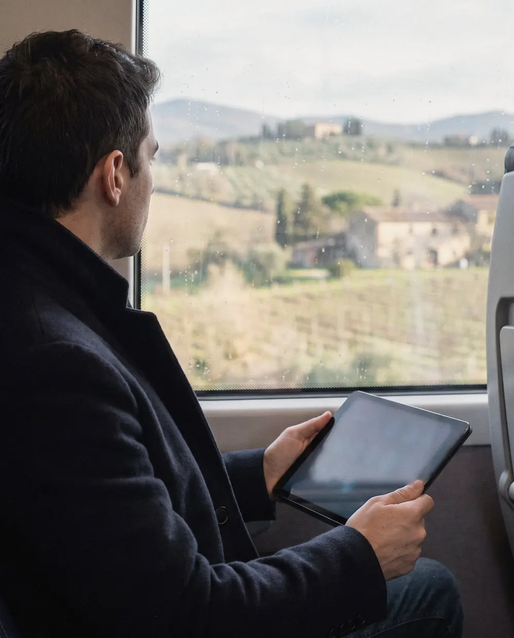 Un manager in treno segue il proprio percorso su un tablet, con la campagna toscana fuori dal finestrino.